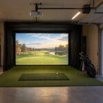 Garage golf simulator with glowing impact screen, open garage door and autumn driveway at dusk